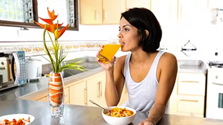 Woman sitting in the kitchen, drinking orange juice